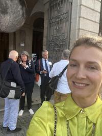 A smiling blonde woman in front of a group of people standing outside a university building